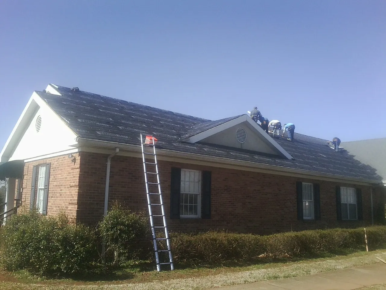 Crew tearing shingles off a brick ranch roof with a ladder set — Metal Roof Repair work by our crew in Electric City