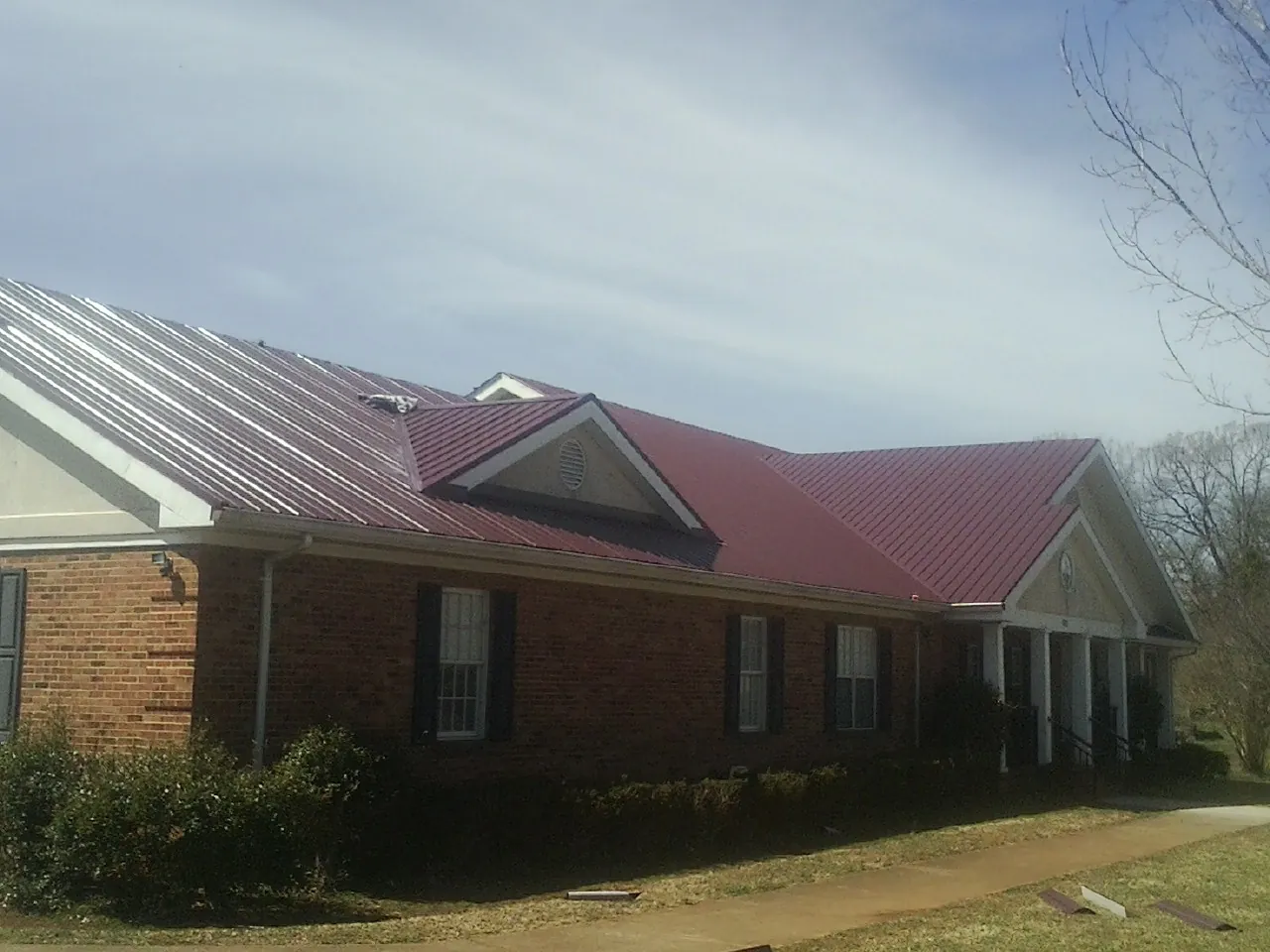 Red metal roof with gabled entries on a long brick building, from a Hail Damage Roof Repair job in Electric City