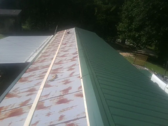 Old rusted panels beside newly installed green metal roofing — Wind Damage Roof Repair by Roofing Brothers in Electric City