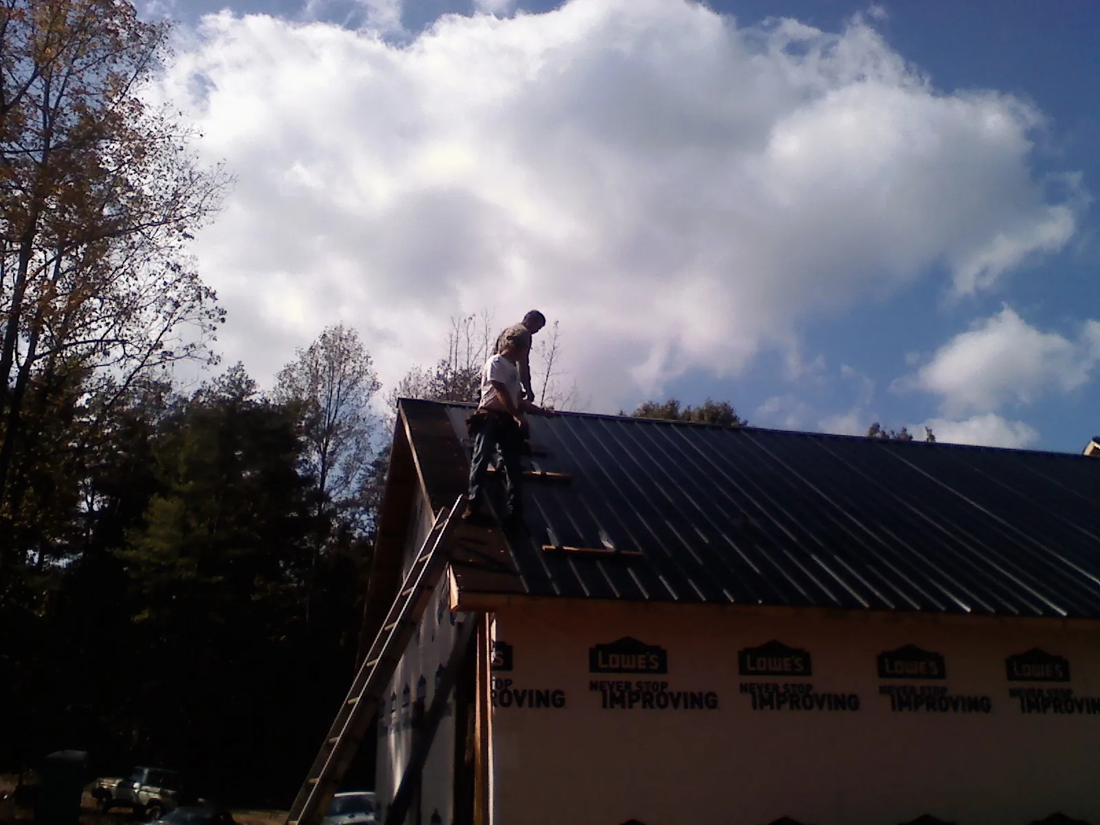 Roofer fastening dark metal panels high against a cloudy sky, from a Roof Inspection job in Electric City