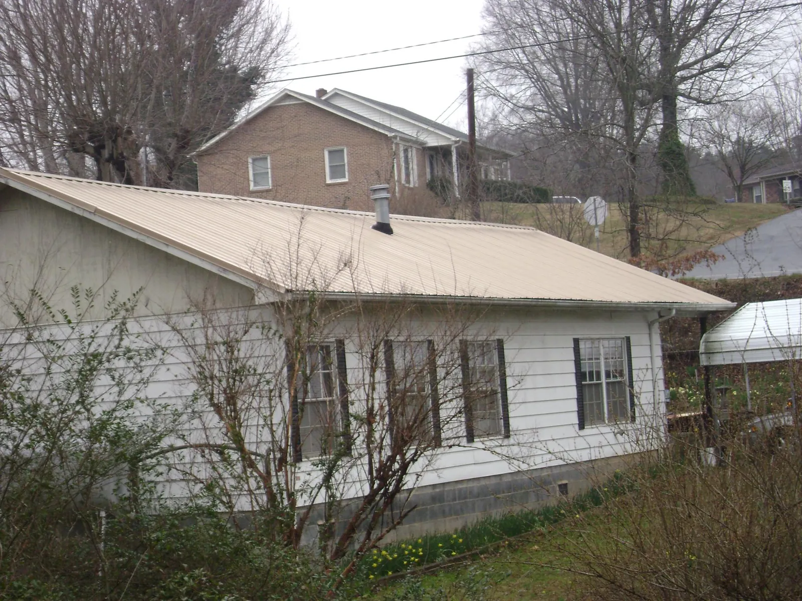 Tan metal roof on a white sided house set into a hillside — Commercial Roofing by Roofing Brothers in Electric City